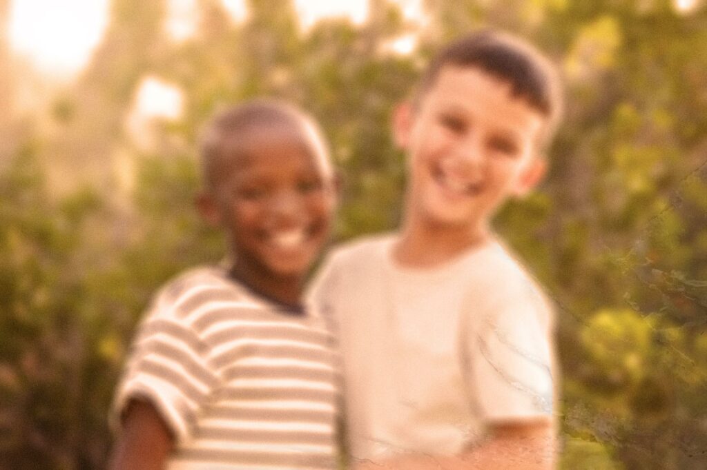 A photo of two boys in front of a stand of trees. The photo's colors are yellow tinted and the image is blurry.